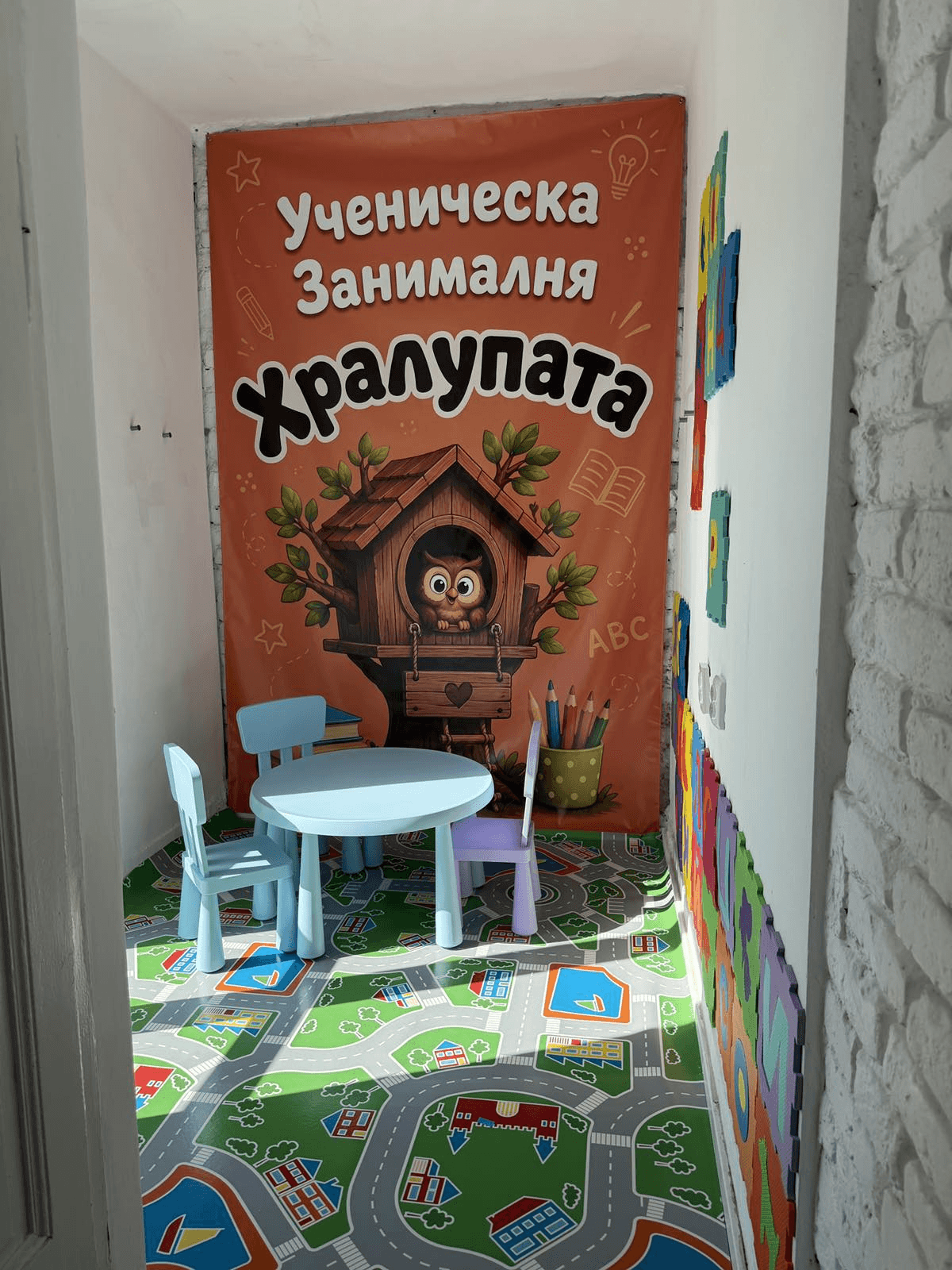 Входът на занималня Хралупата с оранжев банер и бухалче в дървесна къщичка